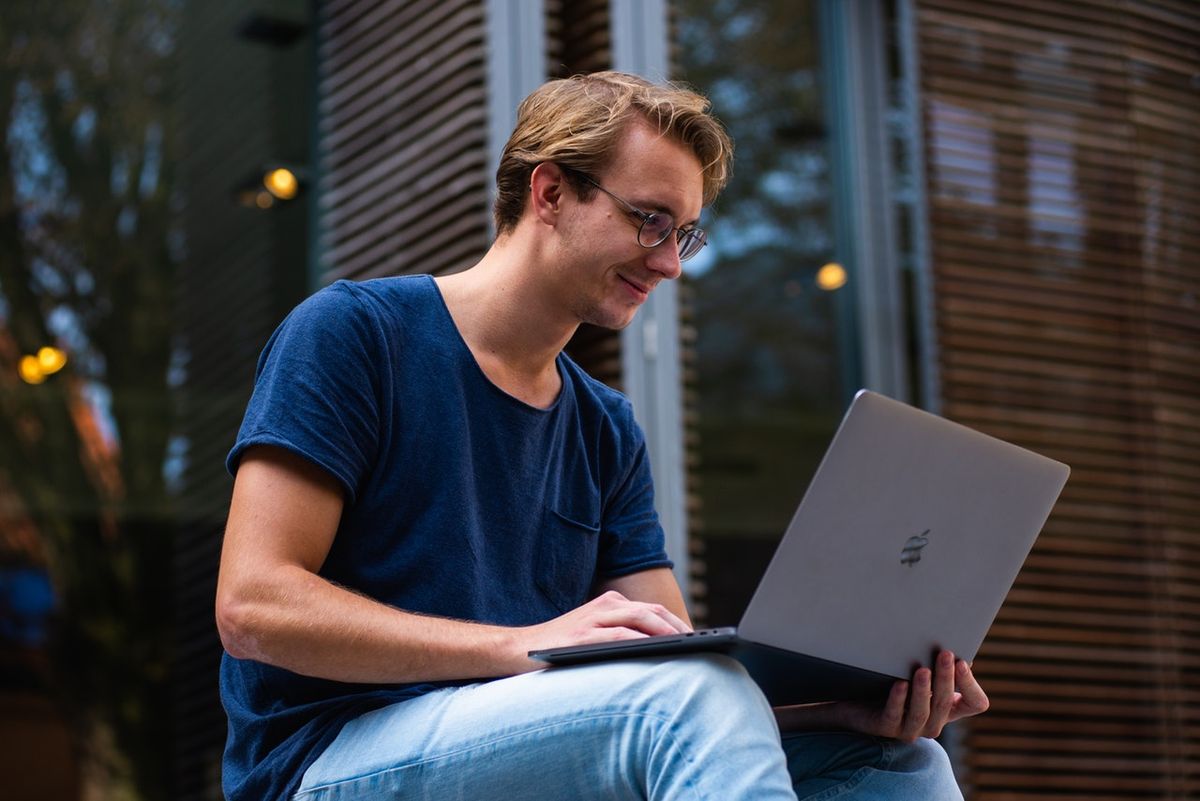 Млад мъж, облечен в дънки и тениска, използва компютъра си Apple навън