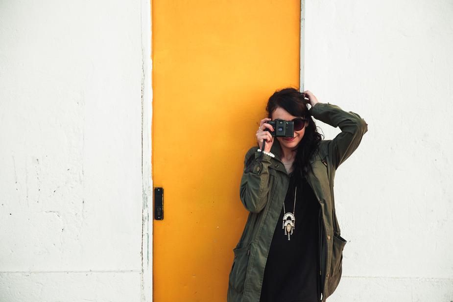 Femme se dresse contre une porte jaune en prenant une photo